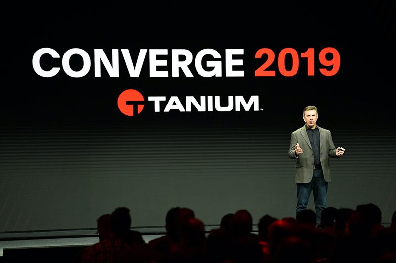 Configuration de l’étape CONVERGE 2019 avec haut-parleur et grands écrans affichant la messagerie Tanium