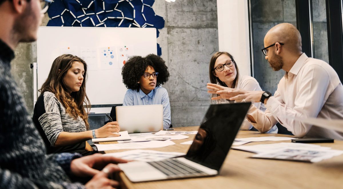 Groupe de personnes collaborant autour d’une table avec des ordinateurs portables et des documents
