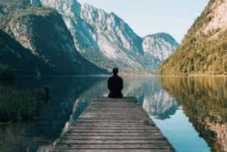 Personne assise sur le quai surplombant le lac de montagne et le paysage boisé