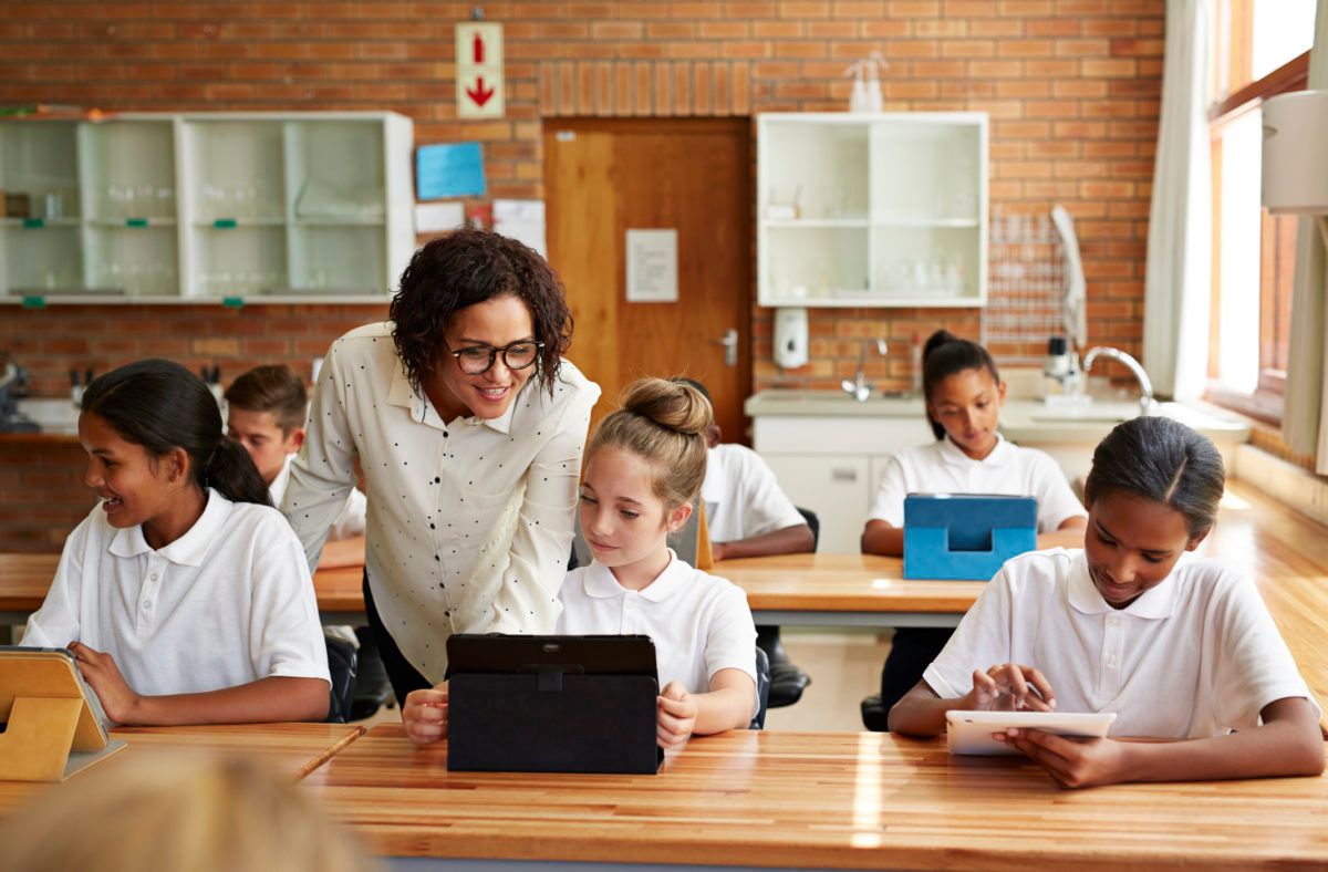 Enseignant aidant les étudiants à leur bureau avec une tablette et des papiers en classe