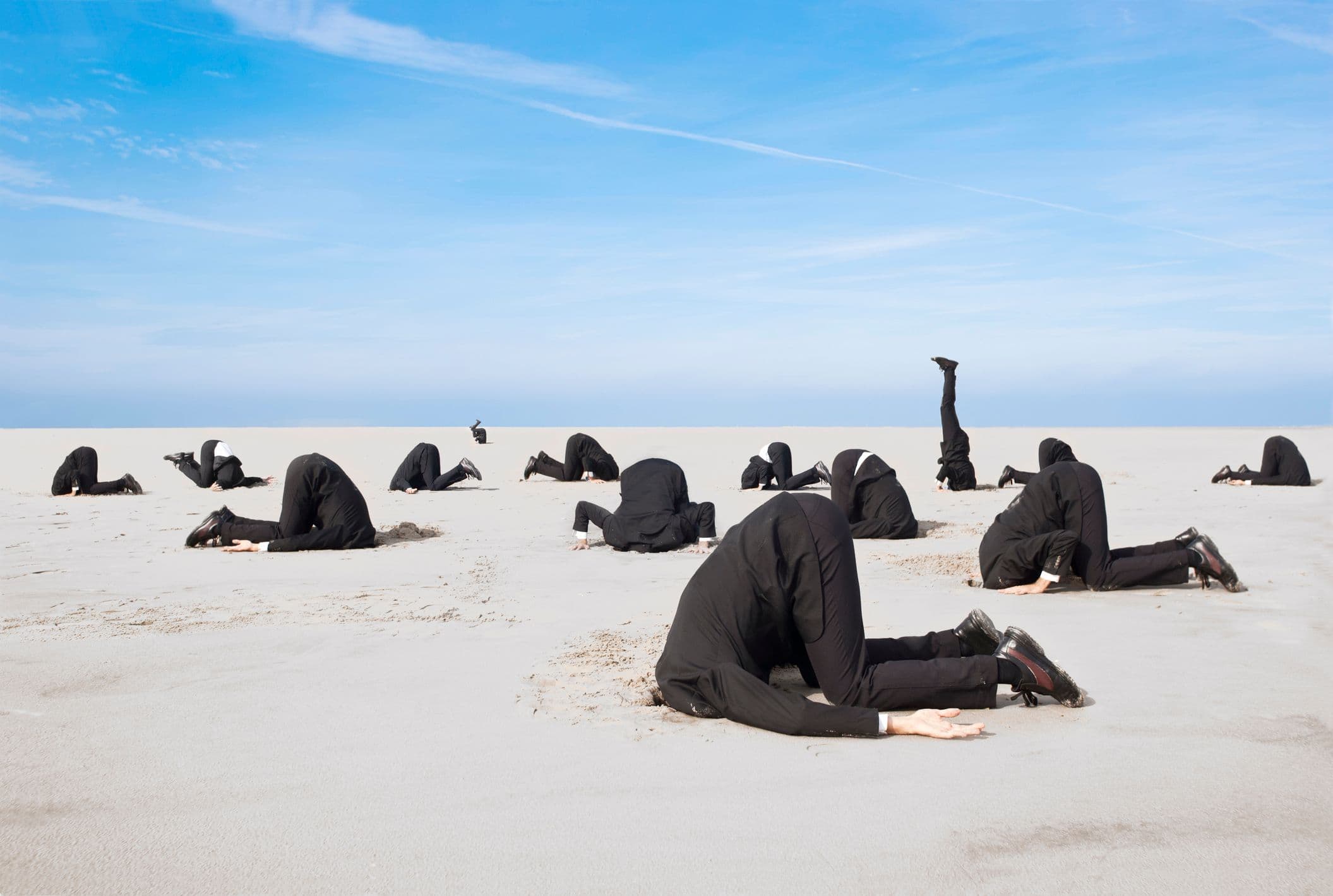 Une photo de cadres en costume, la tête enfoncée dans le sable du désert.