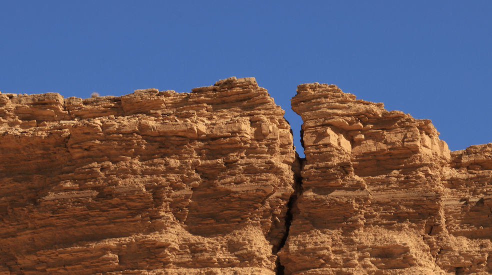 La photo d'une grande fissure verticale dans une falaise rocheuse sous un ciel d'un bleu éclatant.