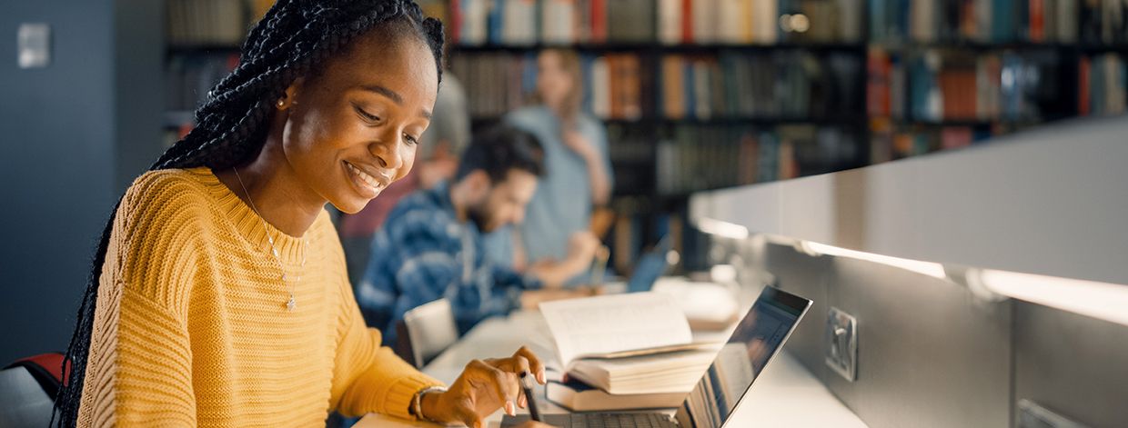 Bibliothèque universitaire : une jeune fille noire douée utilise un ordinateur portable et prend des notes