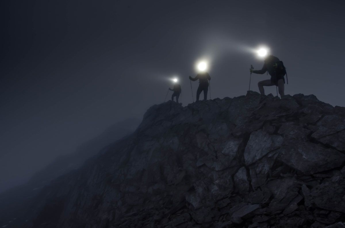 Silhouettes de personnages grimpant des montagnes rocheuses la nuit avec des phares