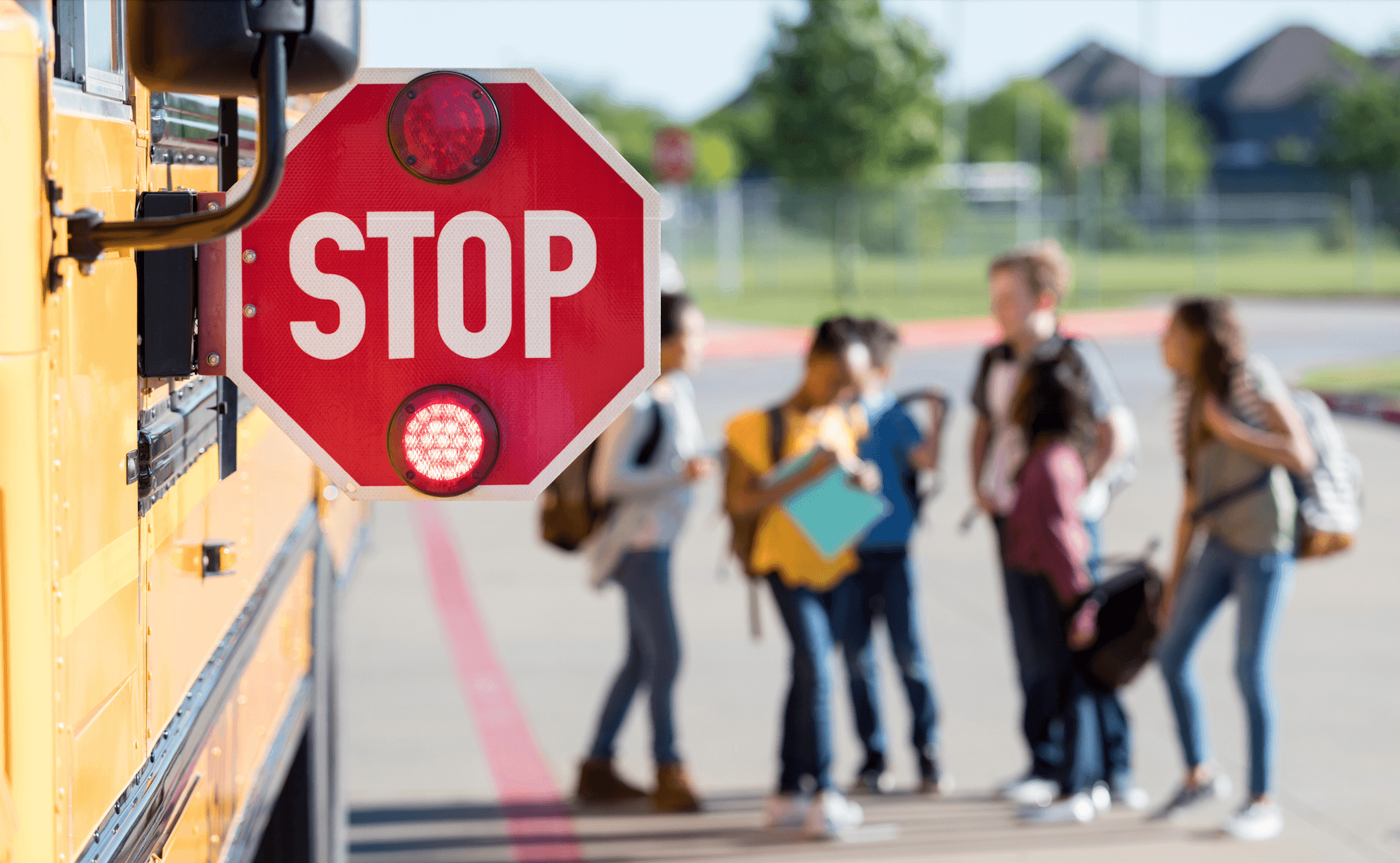 Image vedette du blog. Photo d'un panneau STOP fixé sur le côté d'un bus scolaire, avec des collégiens en train de discuter en arrière-plan.