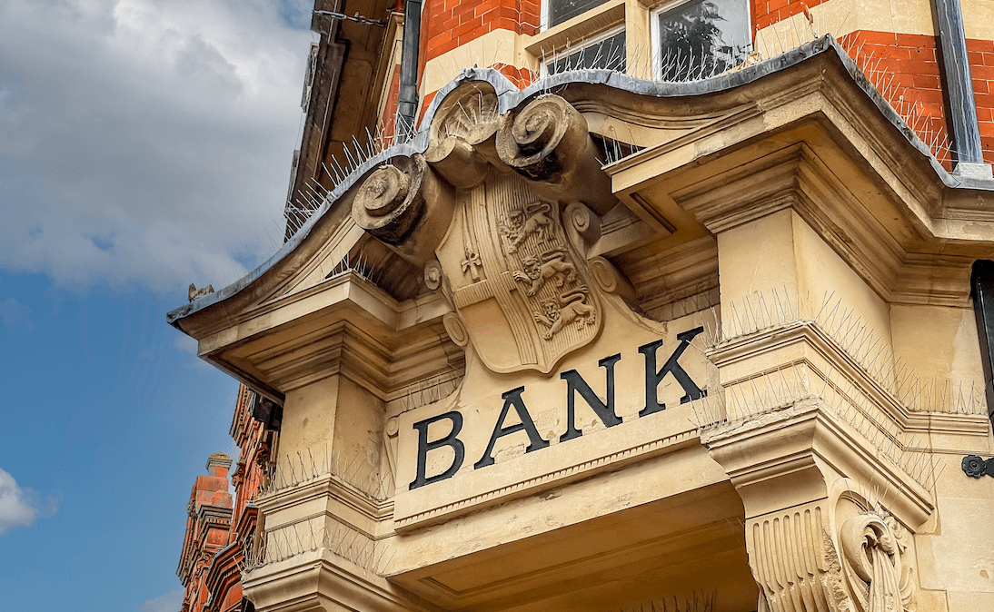 La façade en pierre d'une banque britannique, avec des ornements en volutes et le mot « Bank » gravé au-dessus de l'entrée.