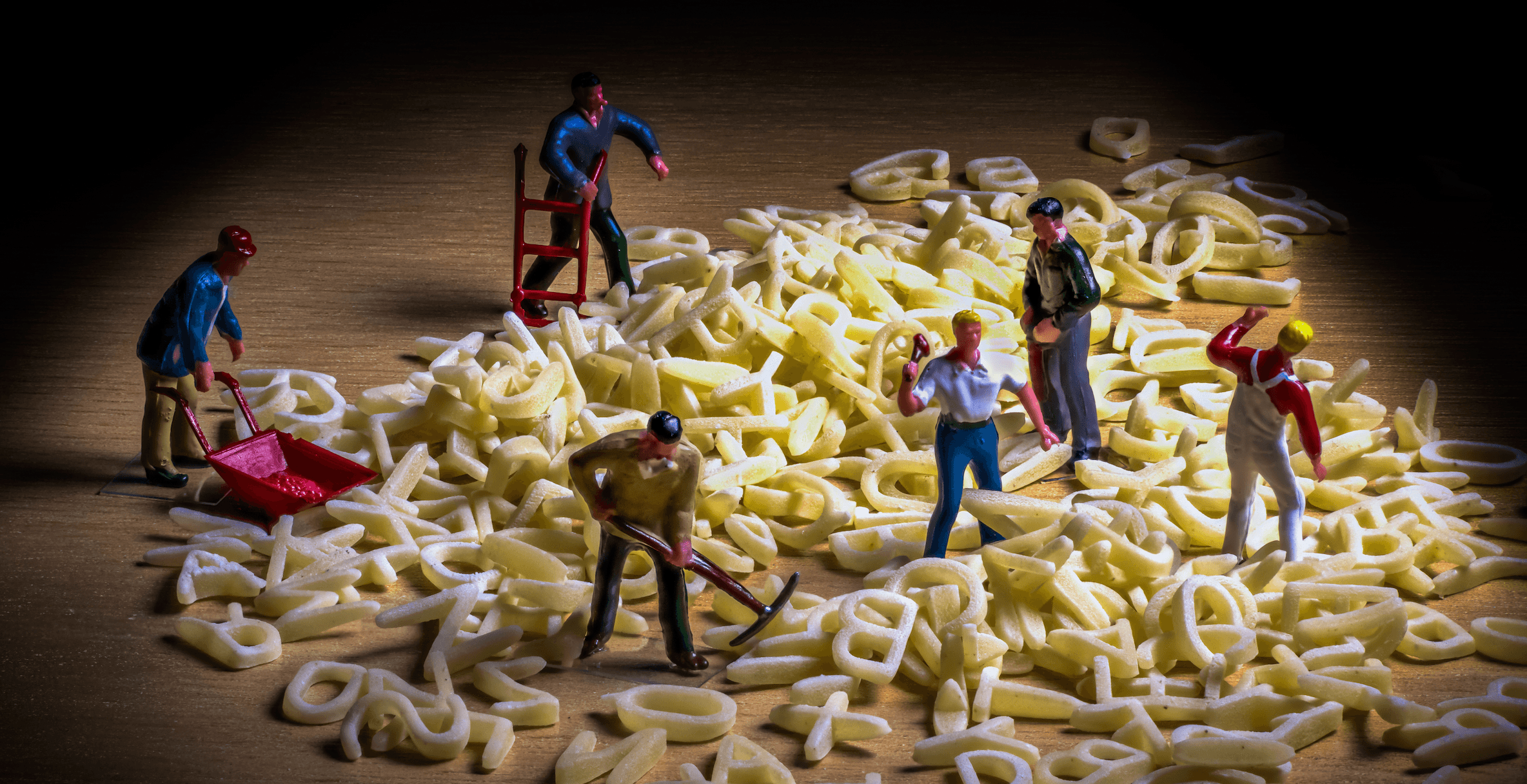 Une photo de figurines miniatures représentant des ouvriers munis de pioches et de brouettes, en train de creuser dans un tas de lettres formant un méli-mélo alphabétique.
