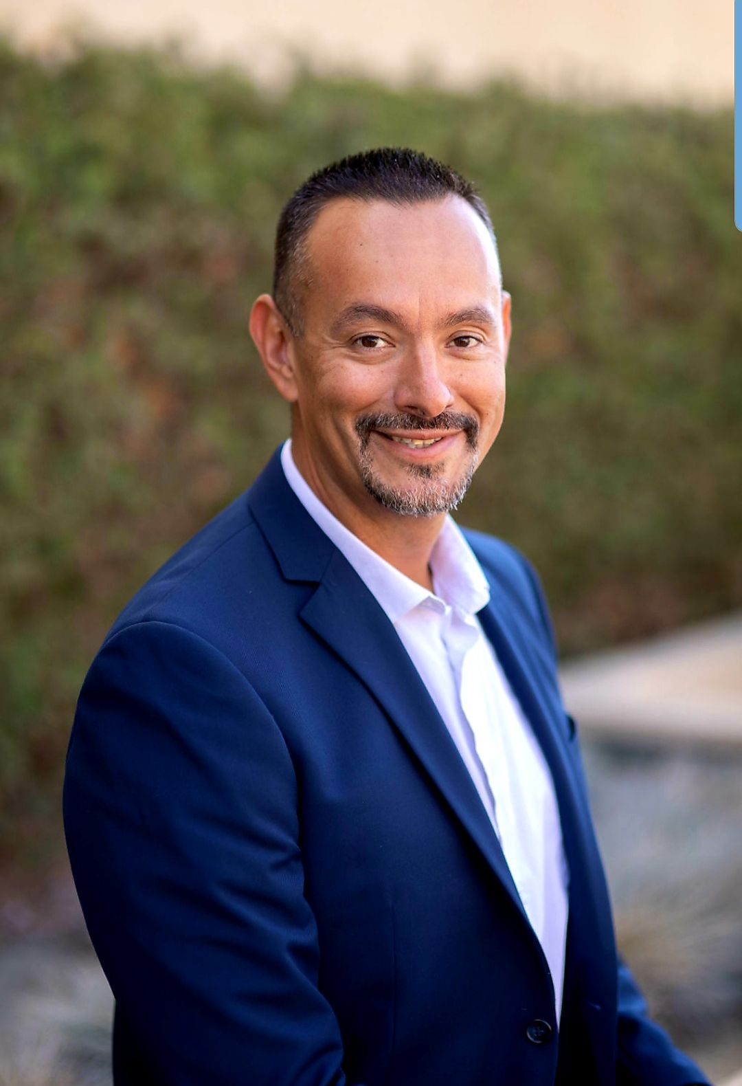 Photo d’un homme de 40 ans, aux cheveux noirs courts, au teint fauve, à la moustache et au menton de 3 jours, affichant un sourire chaleureux.
