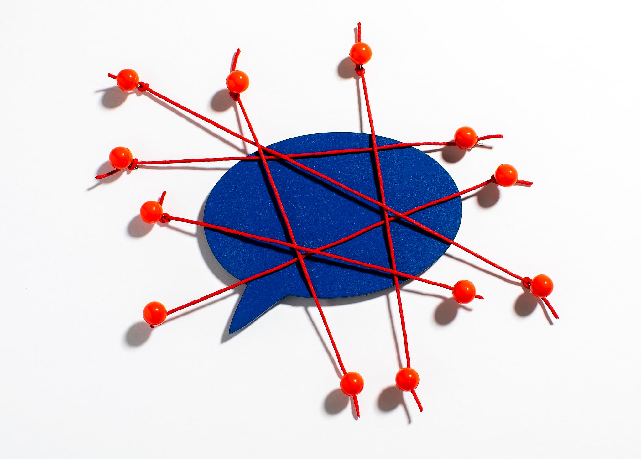 Image représentant une bulle de bande dessinée bleue, enveloppée dans un enchevêtrement de fils rouges et maintenue en place par des punaises.