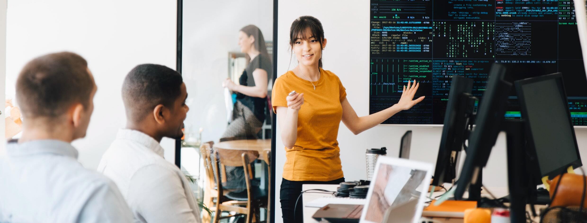 photo de stock d'une femme debout devant un grand écran affichant du code tout en animant une petite réunion