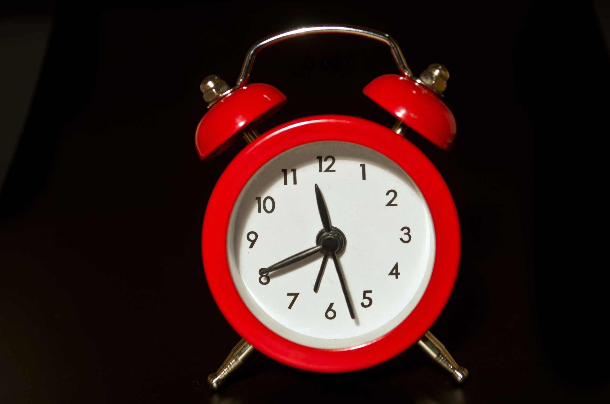 Un réveil rouge vif se détache sur un fond noir — les aiguilles indiquent 11:41.
