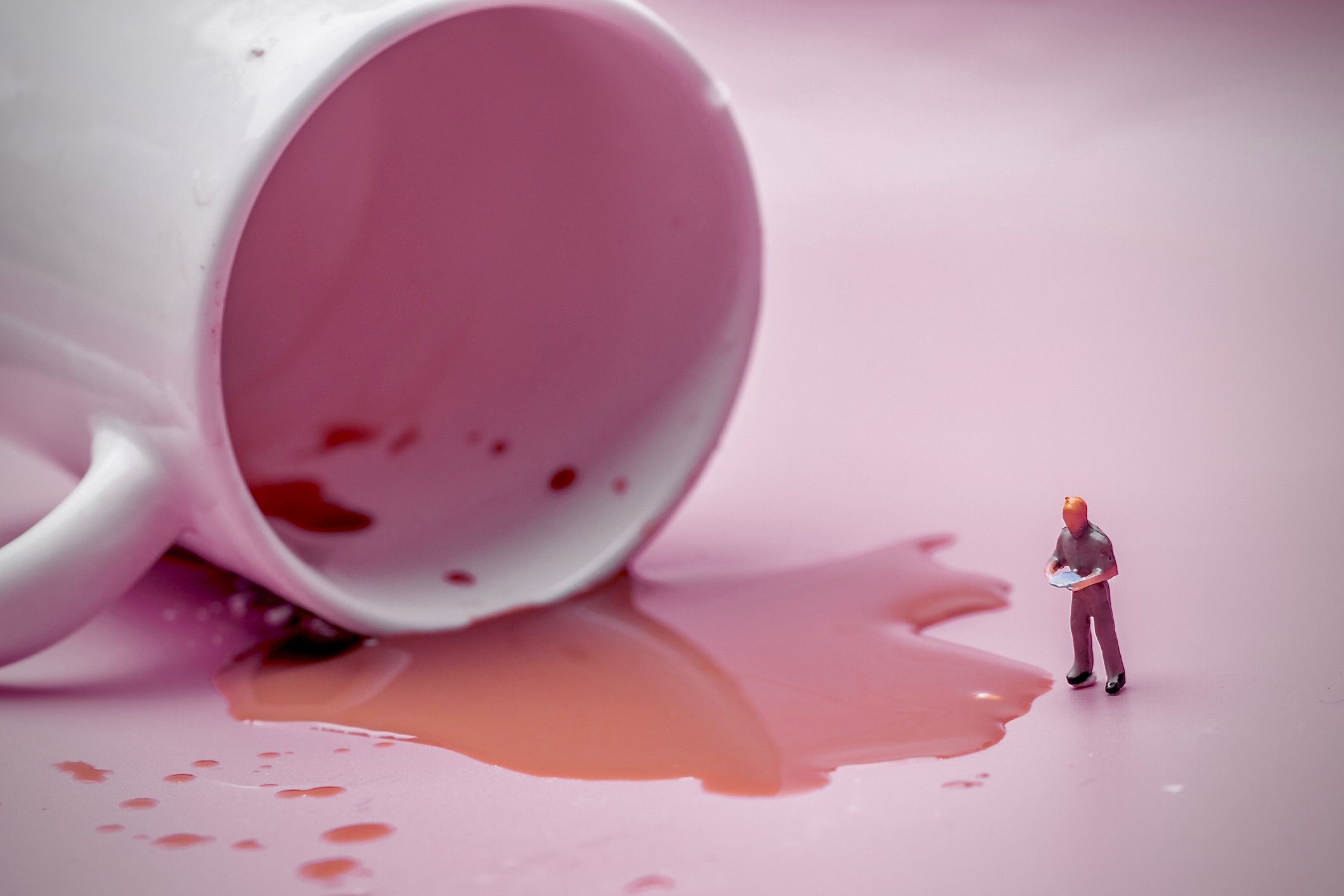 Une image d'une figure humaine miniature évaluant du café renversé provenant d'une tasse retournée.