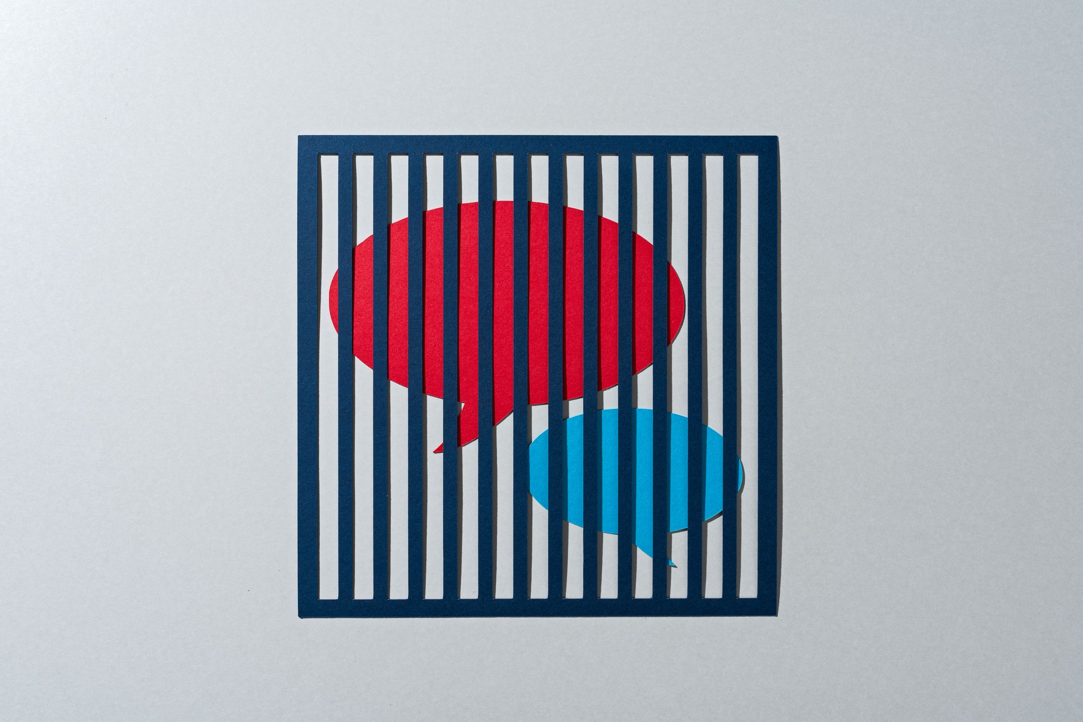 Deux bulles de dialogue, l'une rouge, l'autre turquoise, enfermées derrière des barreaux.