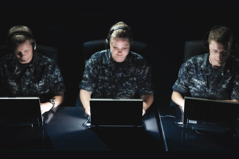 Trois membres du personnel de la Marine en uniformes travaillant sur des ordinateurs